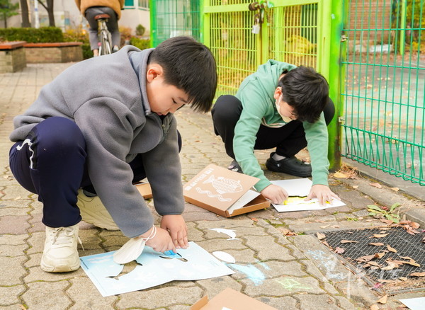 담배꽁초로 가득한 부천 도심 내 빗물받이 근처에서 어린이들이 ‘물살이의 길’ 꾸러미를 활용해 활동을 펼치고 있다.